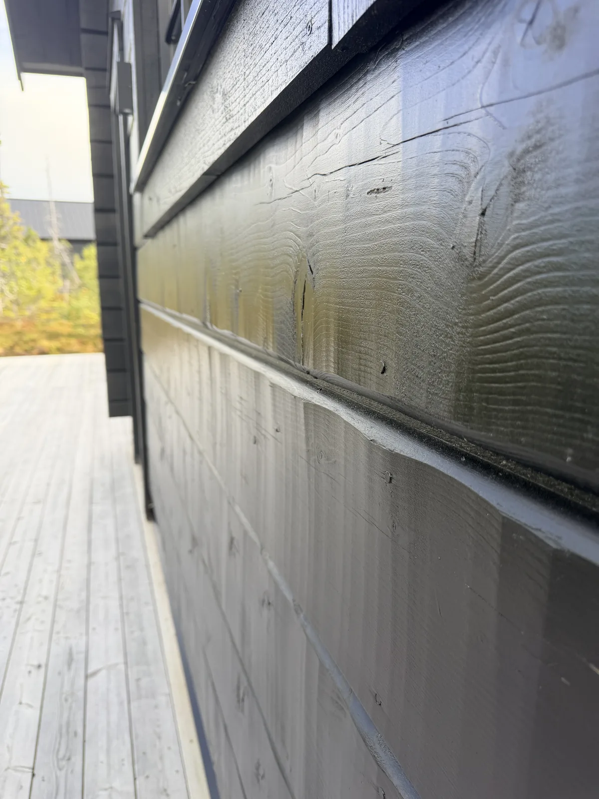 Närbild snett längs svartlaserad fasadpanel där enskilda brädor, ådring och skuggfogar syns
