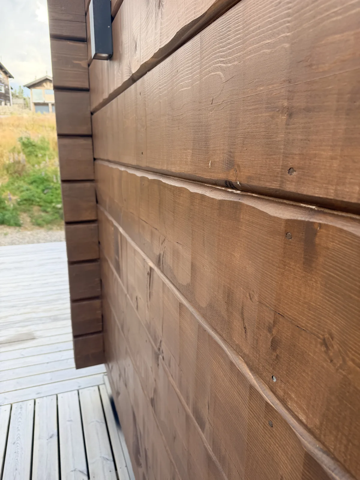 Närbild på brunlaserad fasadpanel med sågad yta och profilerat hörnavslut mot knuten